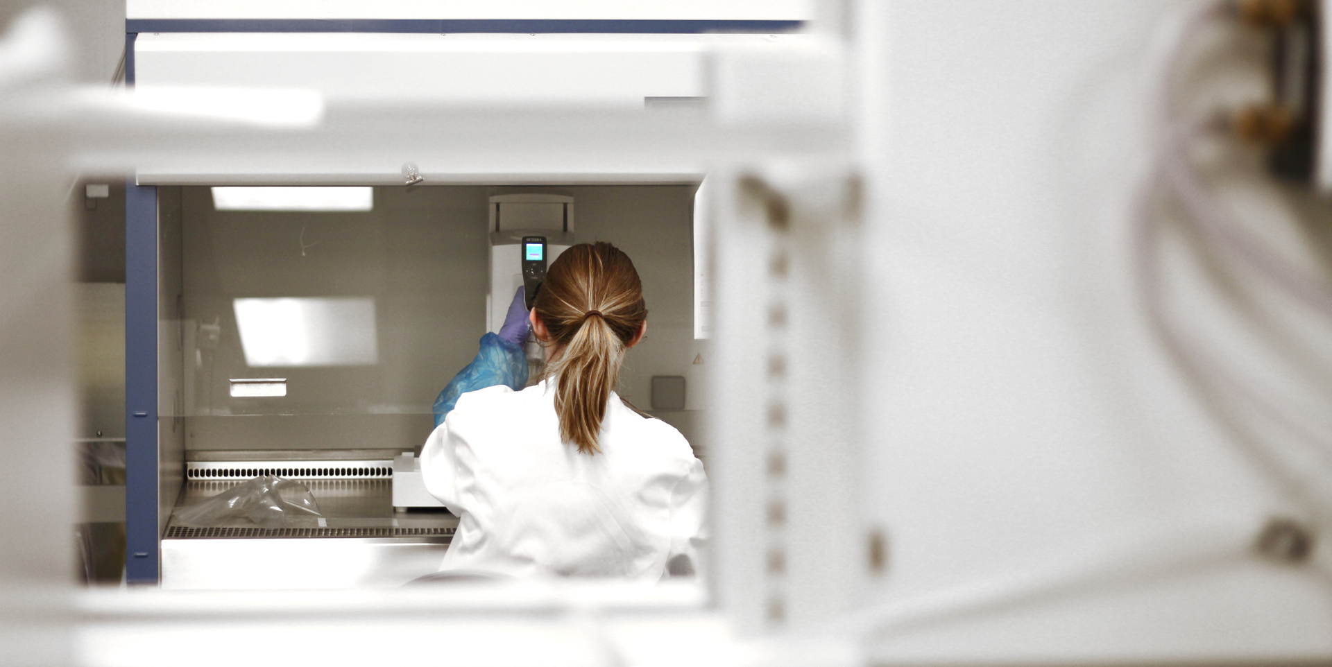 Lab Space for Start-Ups: image depicts a woman working in a laboratory. She is wearing a white lab coat and gloves and has her back to the camera.