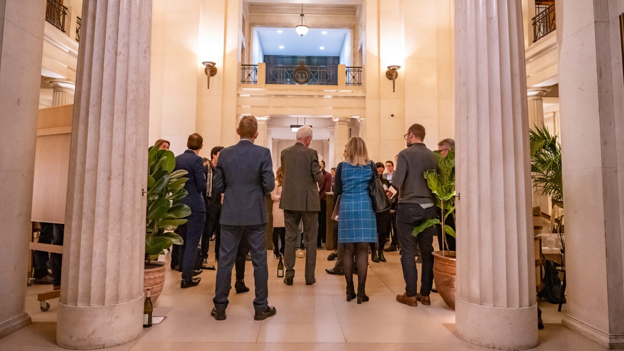 Guests at an event, standing in Victoria House, listening to a speaker.