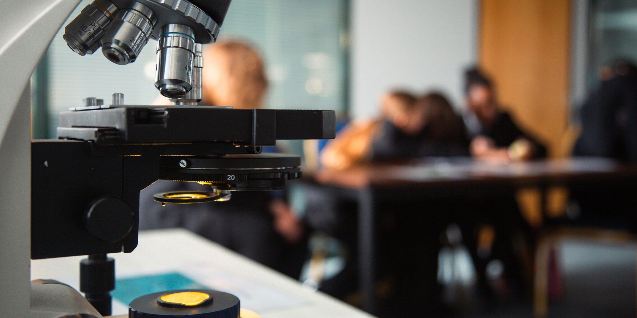 A microscope in focus with school children working in the background out of focus.